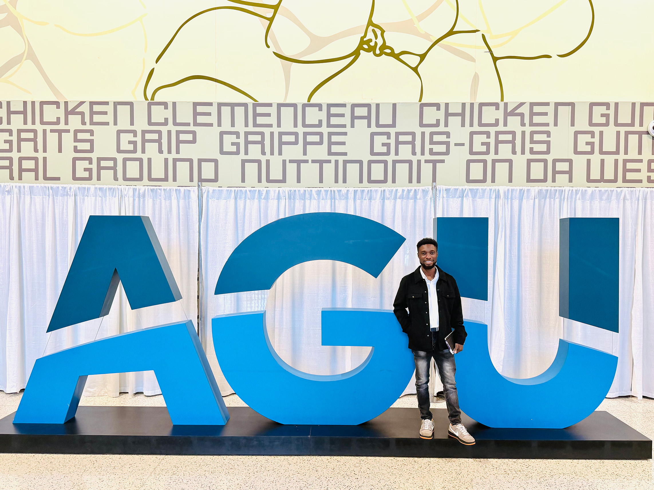 Isaac stands in front of the AGU sign at AGU 2025